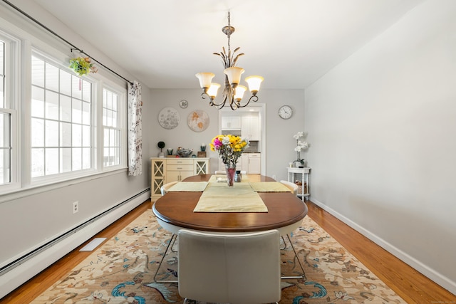 dining space featuring light wood finished floors, a baseboard radiator, baseboards, and a notable chandelier