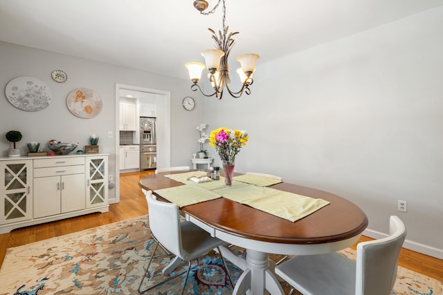 dining room featuring baseboards, light wood finished floors, and a notable chandelier