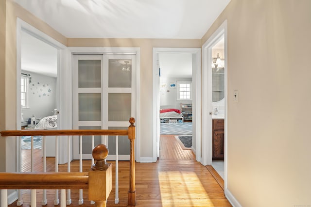 corridor with light wood-style flooring, baseboards, and a sink