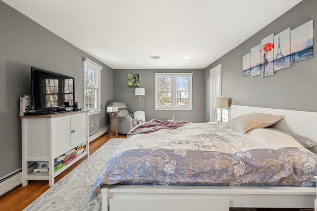 bedroom featuring baseboard heating, visible vents, multiple windows, and wood finished floors