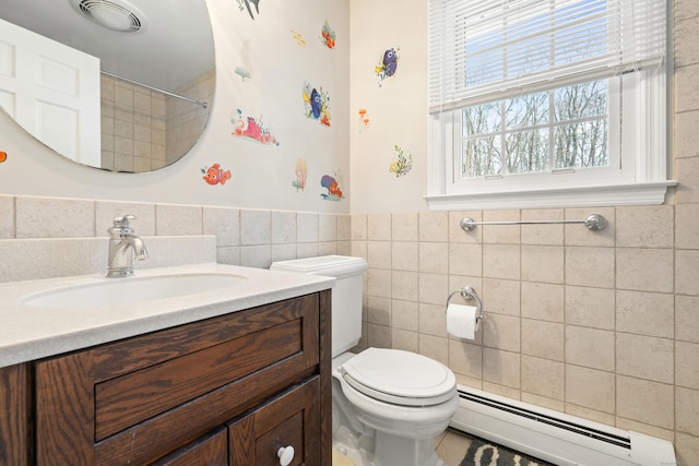 bathroom with toilet, vanity, tile walls, baseboard heating, and wainscoting