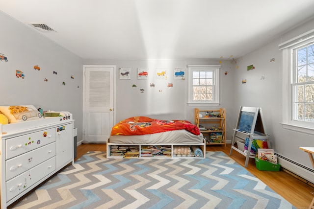 bedroom with baseboard heating, multiple windows, visible vents, and light wood finished floors