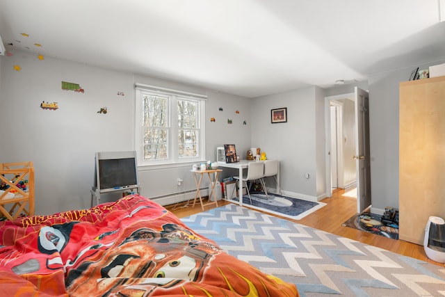 bedroom with a baseboard heating unit, light wood-style flooring, and baseboards