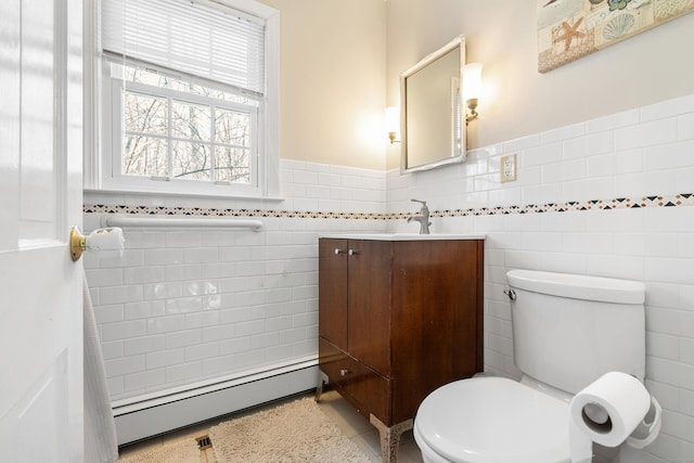 bathroom featuring tile walls, toilet, baseboard heating, wainscoting, and vanity