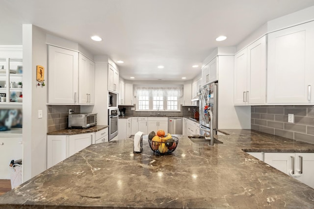 kitchen featuring a peninsula, a sink, white cabinetry, appliances with stainless steel finishes, and dark stone counters