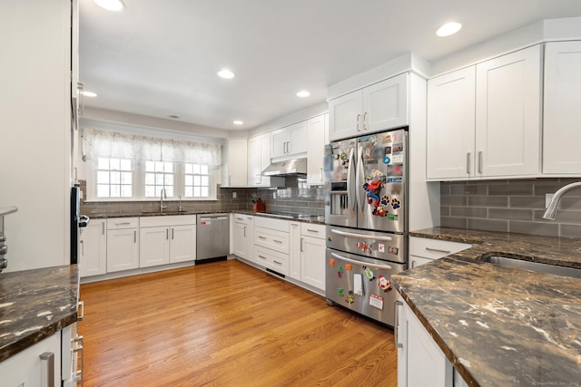 kitchen featuring appliances with stainless steel finishes, a sink, under cabinet range hood, and light wood finished floors