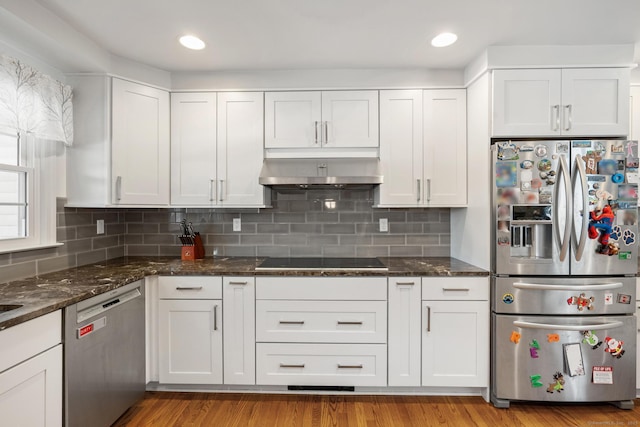 kitchen featuring dark stone counters, stainless steel appliances, ventilation hood, and white cabinetry