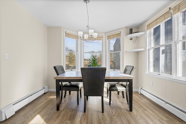 dining room with a chandelier, light wood finished floors, baseboard heating, and baseboards