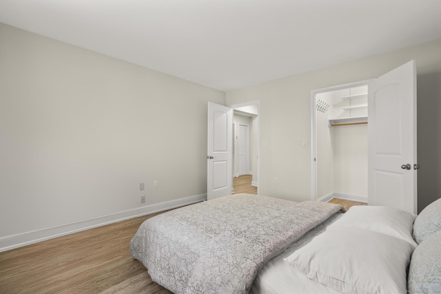 bedroom featuring light wood-style flooring, baseboards, a walk in closet, and a closet