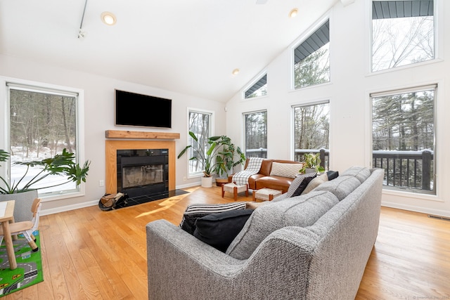 living room with high vaulted ceiling, a fireplace with flush hearth, visible vents, baseboards, and wood-type flooring