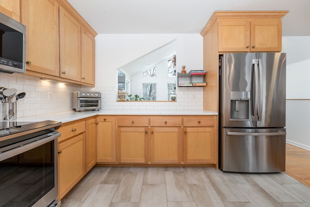 kitchen featuring tasteful backsplash, light countertops, appliances with stainless steel finishes, light brown cabinets, and vaulted ceiling