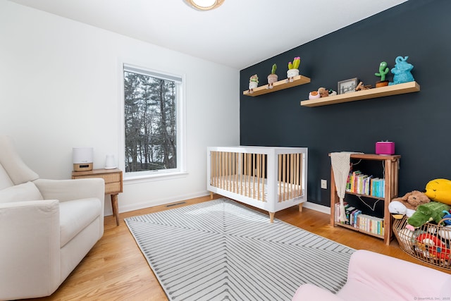 bedroom featuring baseboards, visible vents, an accent wall, a nursery area, and light wood-style floors