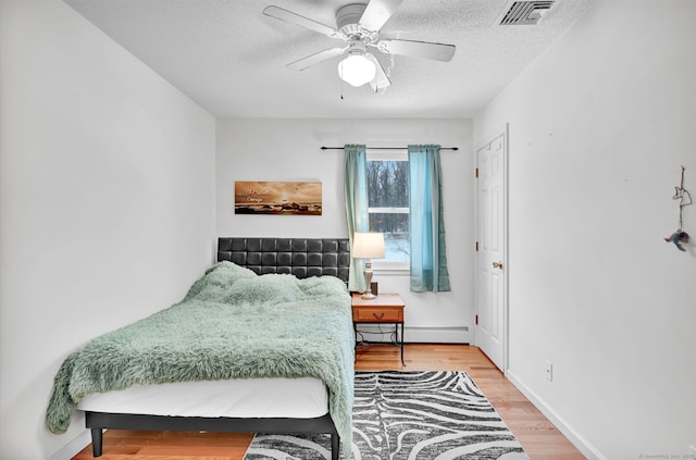 bedroom with ceiling fan, hardwood / wood-style floors, a textured ceiling, and a baseboard heating unit