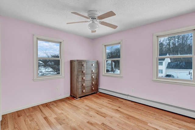 unfurnished bedroom with multiple windows, a baseboard radiator, a textured ceiling, and light hardwood / wood-style floors