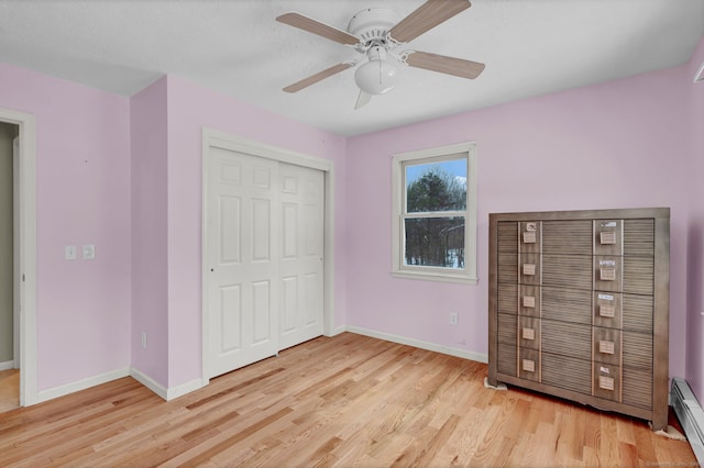 unfurnished bedroom featuring a closet, a baseboard heating unit, ceiling fan, and light hardwood / wood-style flooring