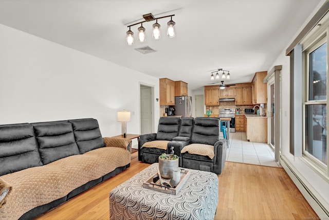 living room featuring rail lighting, light hardwood / wood-style flooring, and a baseboard heating unit