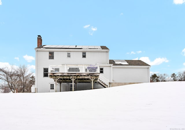 snow covered house featuring a deck and solar panels