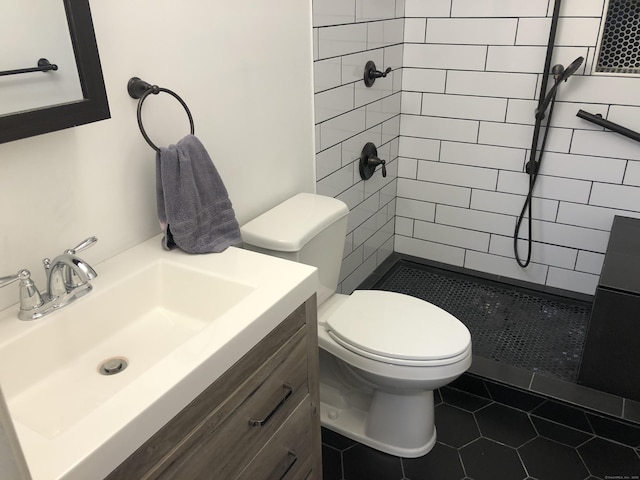 bathroom with tiled shower, vanity, toilet, and tile patterned flooring