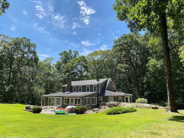 rear view of house with a sunroom, a patio, a chimney, and a lawn