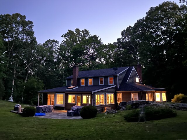 rear view of house featuring a patio area, a lawn, and a chimney