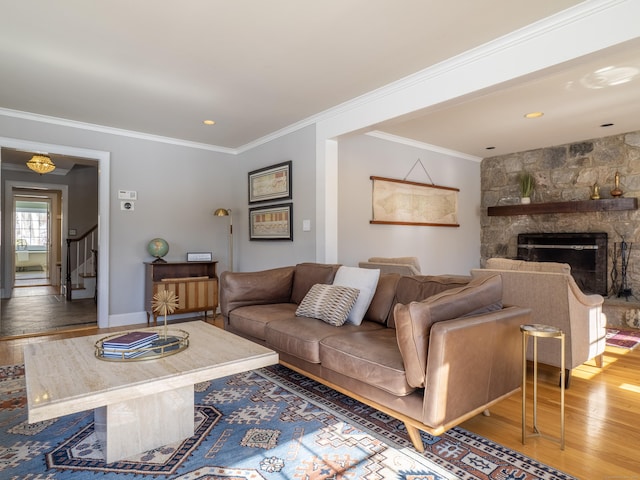 living room featuring a stone fireplace, wood finished floors, baseboards, stairs, and ornamental molding