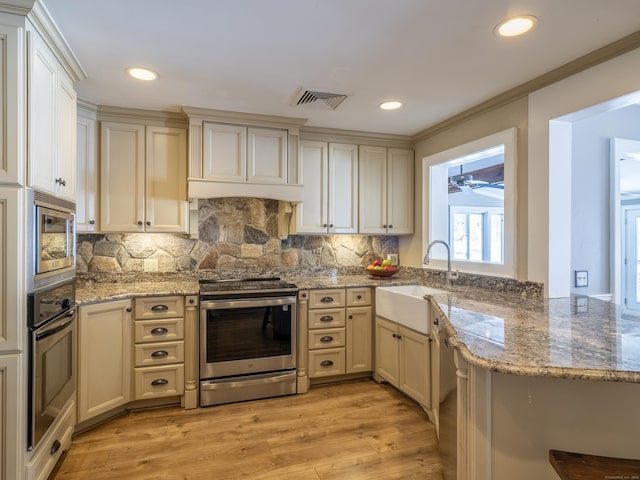 kitchen featuring a sink, appliances with stainless steel finishes, light wood-type flooring, light stone countertops, and tasteful backsplash