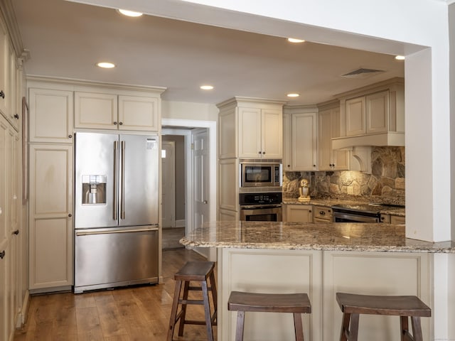 kitchen featuring stainless steel appliances, light stone counters, a peninsula, and a breakfast bar