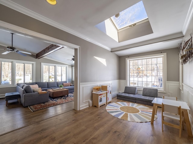 living area featuring lofted ceiling with skylight, crown molding, wood finished floors, and wainscoting