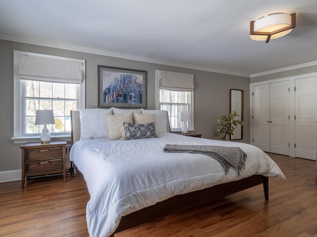 bedroom with two closets, crown molding, and wood finished floors