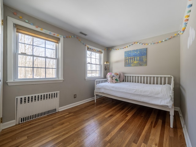 bedroom with baseboards, visible vents, radiator heating unit, and wood finished floors