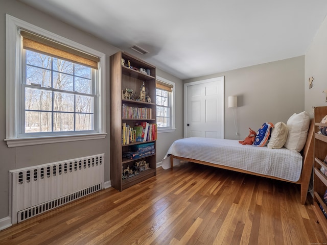 bedroom with radiator heating unit, wood finished floors, visible vents, and baseboards