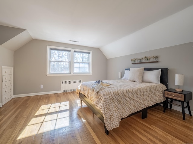 bedroom with vaulted ceiling, light wood-style floors, visible vents, and radiator