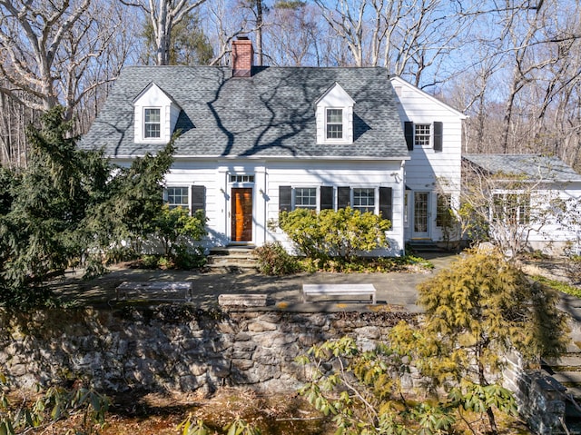 new england style home featuring roof with shingles and a chimney