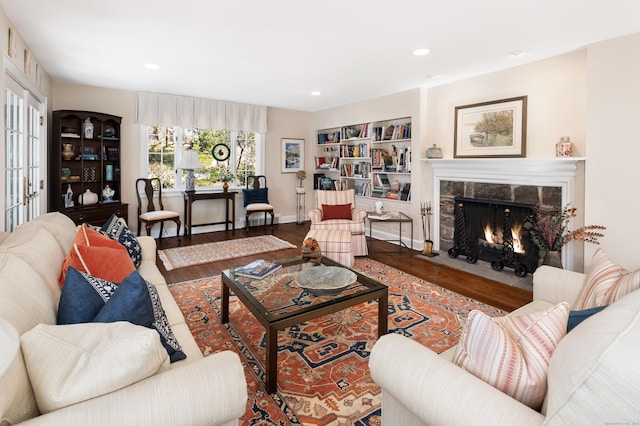 living room with built in shelves, wood finished floors, baseboards, a fireplace, and recessed lighting