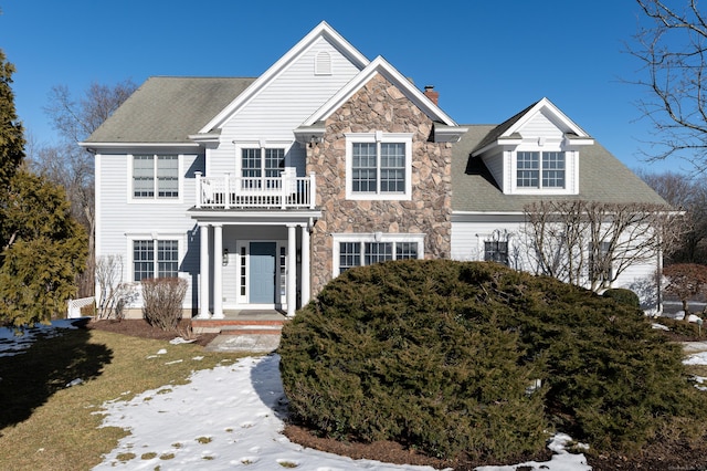 view of front of home with a chimney, stone siding, roof with shingles, and a balcony