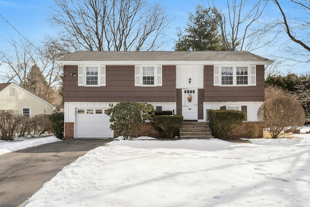 raised ranch featuring board and batten siding, a garage, brick siding, and driveway