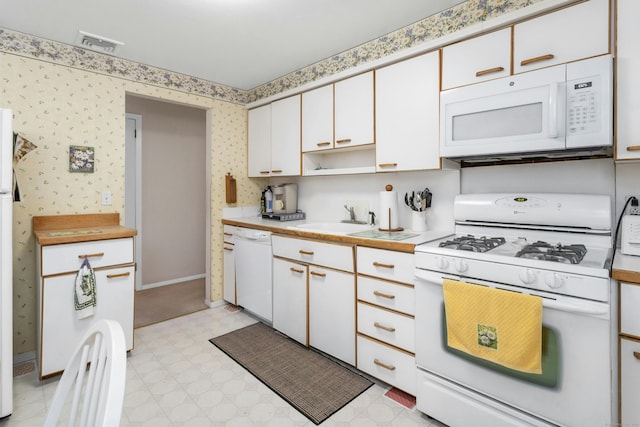 kitchen with white appliances, light floors, visible vents, wallpapered walls, and light countertops