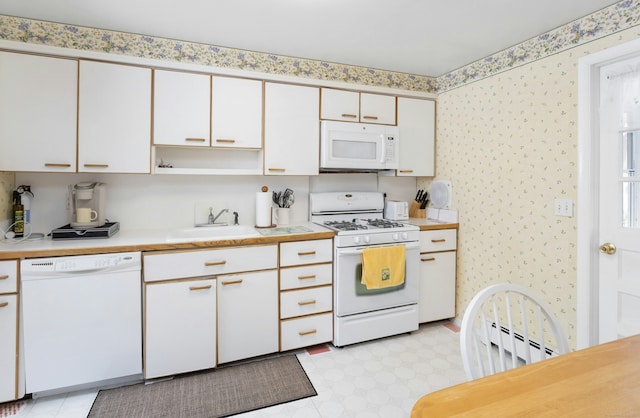 kitchen featuring wallpapered walls, light floors, light countertops, white appliances, and a sink