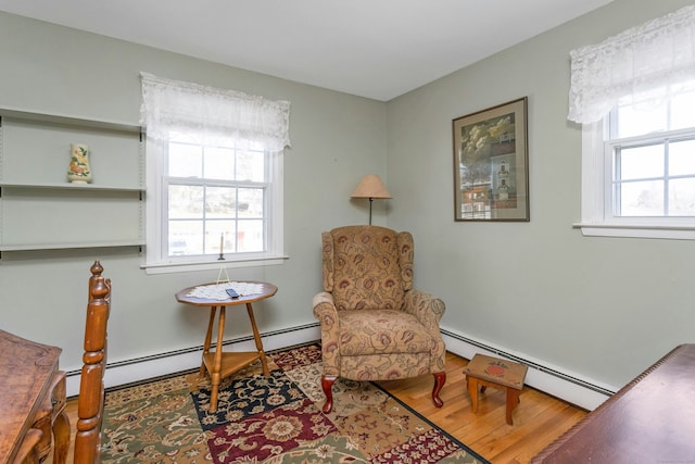 living area with a baseboard radiator, a healthy amount of sunlight, and wood finished floors