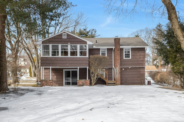 snow covered rear of property featuring a chimney and roof with shingles