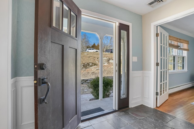 foyer entrance featuring a wainscoted wall, crown molding, visible vents, a decorative wall, and a baseboard heating unit