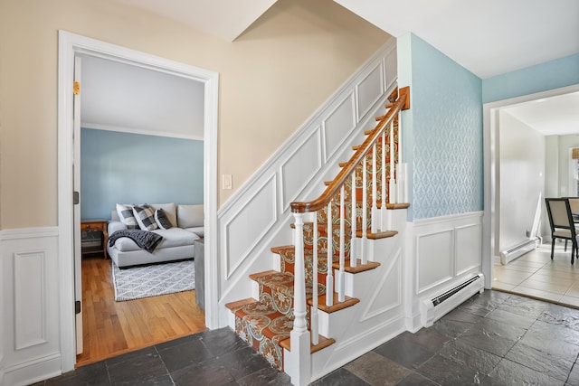 stairs with baseboard heating, wainscoting, and stone tile flooring