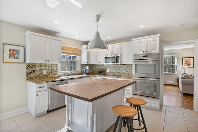 kitchen featuring light tile patterned floors, butcher block countertops, appliances with stainless steel finishes, white cabinetry, and a sink