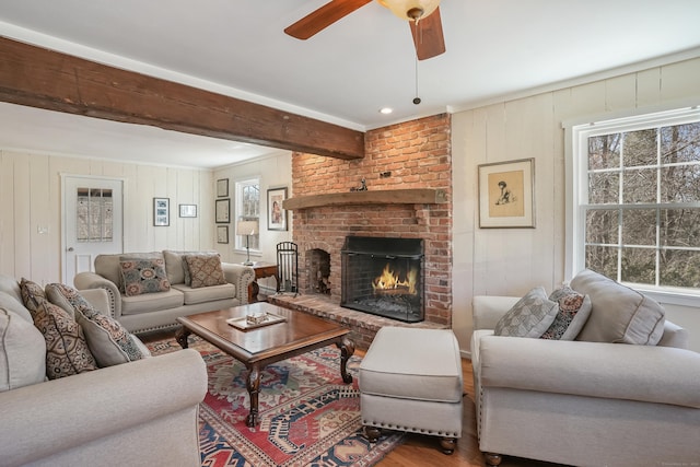 living area with a brick fireplace, a ceiling fan, beamed ceiling, and wood finished floors