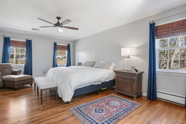 bedroom with a ceiling fan, visible vents, a baseboard heating unit, and light wood-style flooring