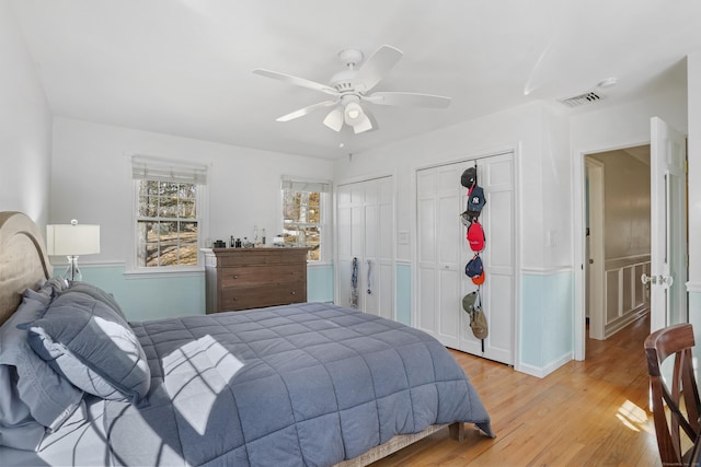 bedroom featuring a ceiling fan, light wood-type flooring, visible vents, and two closets