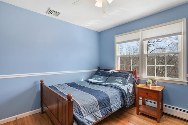 bedroom with baseboards, visible vents, a ceiling fan, wood finished floors, and baseboard heating