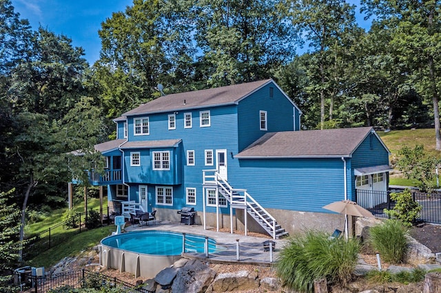 rear view of property with a fenced backyard, a shingled roof, stairway, a fenced in pool, and a patio area