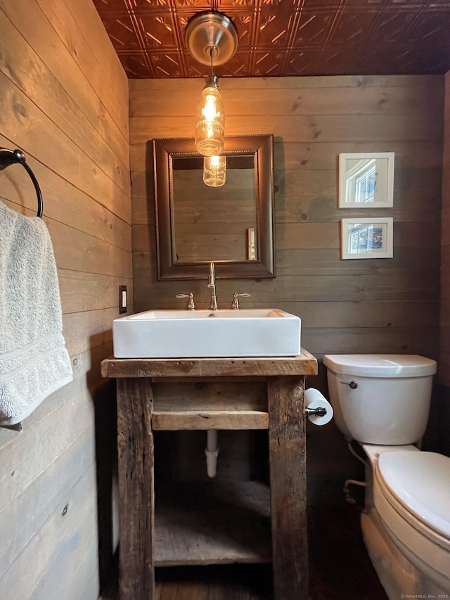 bathroom with toilet, wood walls, an ornate ceiling, and a sink