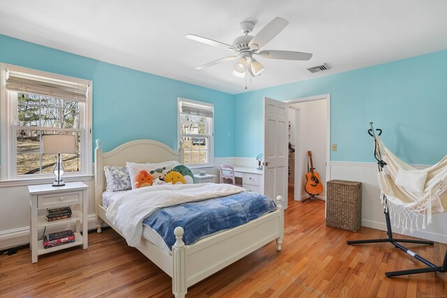 bedroom with light wood-style floors, wainscoting, ceiling fan, and visible vents